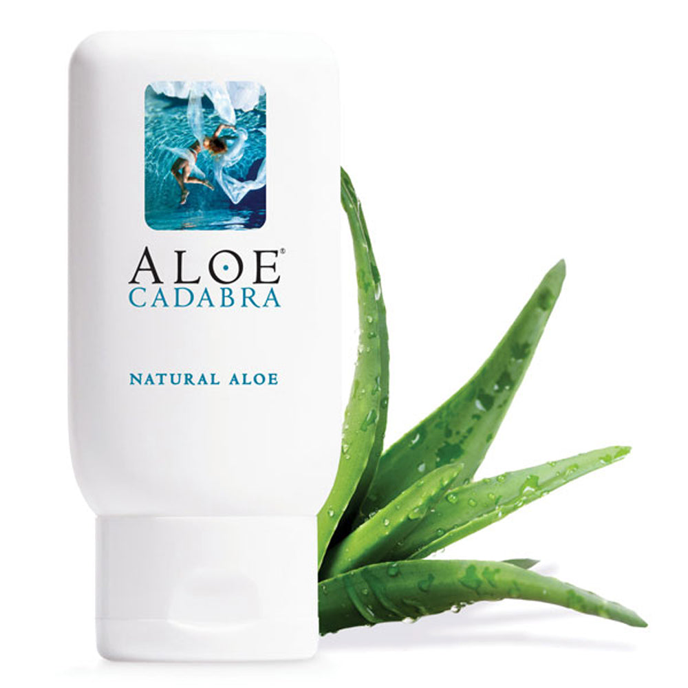 A bottle of Aloe Cadabra, a natural aloe based lubricant with an image of a woman swimming underwater. The packaging is white with blue text. An aloe vera plant is next to the bottle.