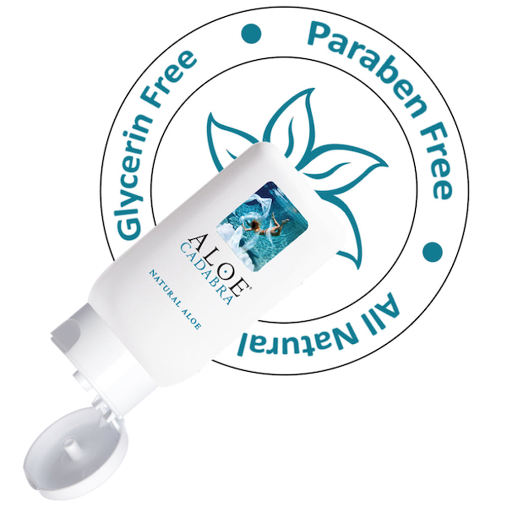 An opened bottle of Aloe Cadabra, a natural aloe based lubricant with an image of a woman swimming underwater. The packaging is white with blue text. Behind the bottle is a label that describes that the product is all natural and free of glycerin and paraben.