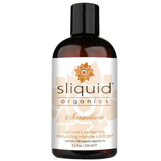 Bottle of Sliquid Organics Sensation Water Based Lube with a label showing the brand name and product name, alongside a graphic of a flower and leaves. The bottle is transparent, revealing the amber-colored lubricant inside.