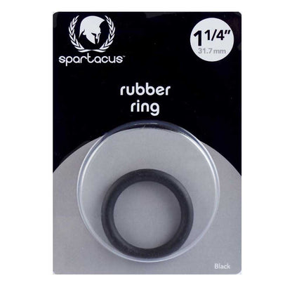 A black rubber cock ring by Spartacus, packaged in a clear plastic case with a black and white label. The ring is visible through the case, indicating a snug fit for controlling ejaculation and enhancing performance.